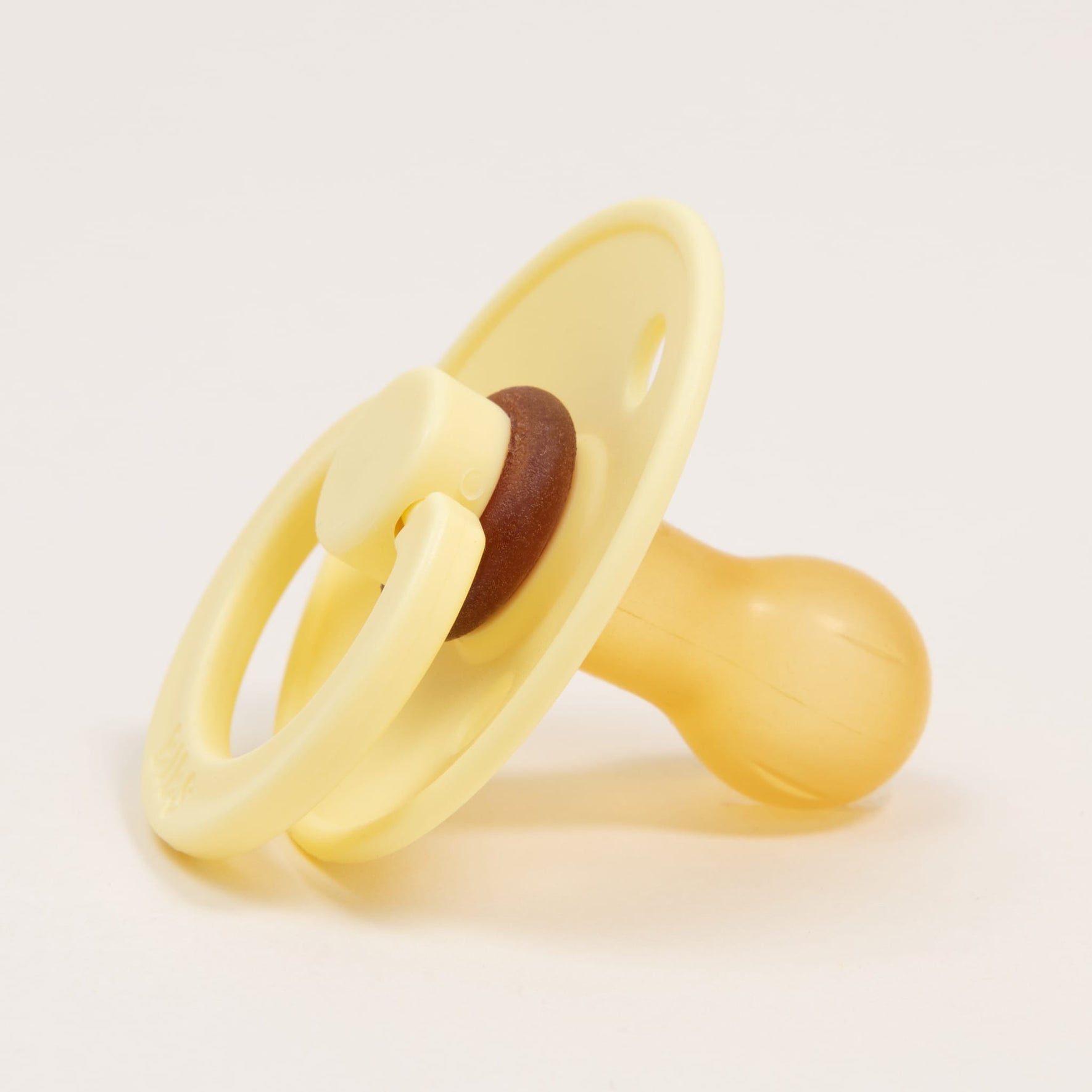 A Bibs Pacifier from the Sunshine 2 Pack, made of classic yellow natural rubber with a round handle, rests on a neutral background. Its soft, rounded nipple and small circular shield are designed to help babies self-soothe comfortably.