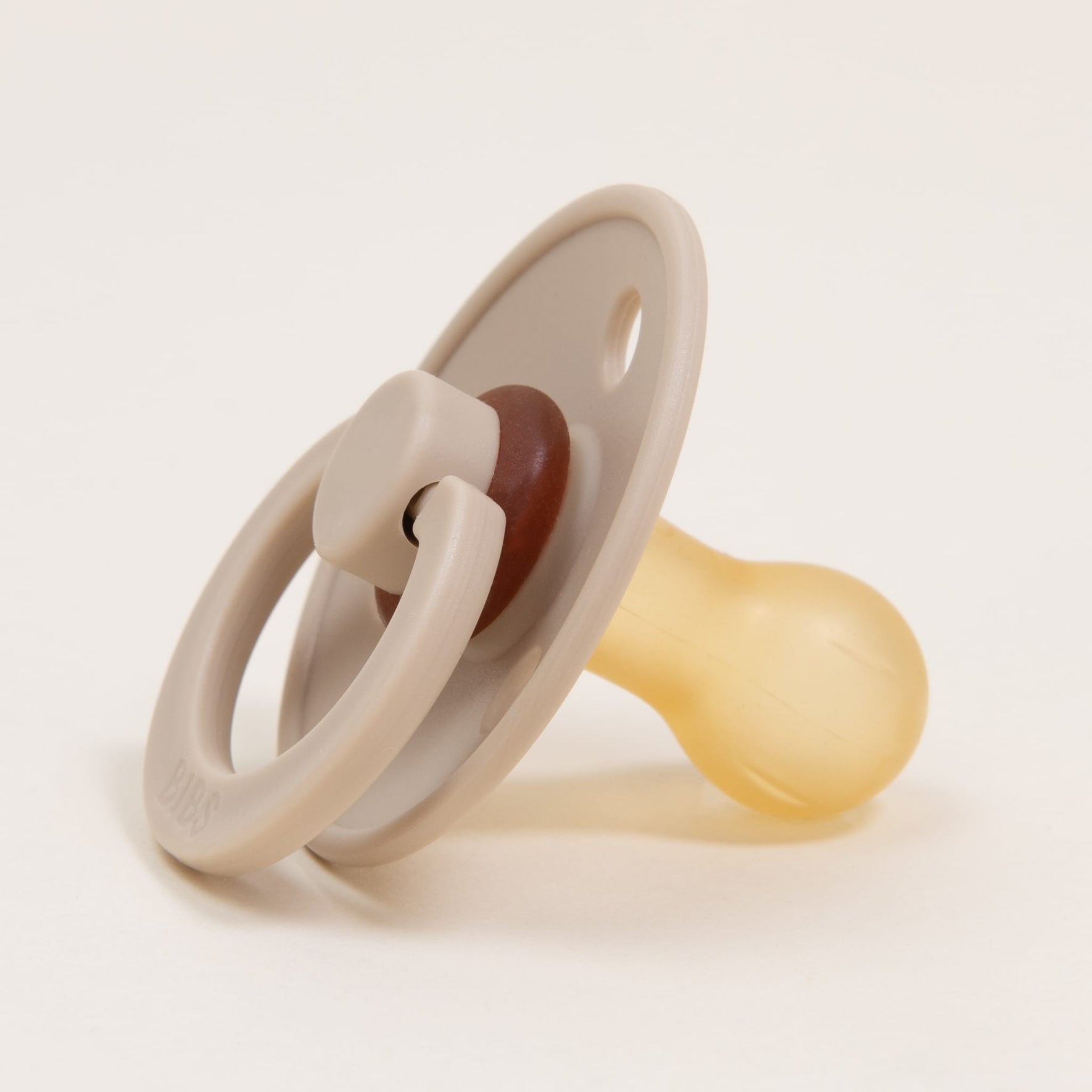 The Bibs Pacifier 2 Pack in Vanilla offers a classic look with a beige round shield and ring handle, complemented by a yellow natural rubber nipple. Made in Denmark, these pacifiers are elegantly displayed against a plain white background.