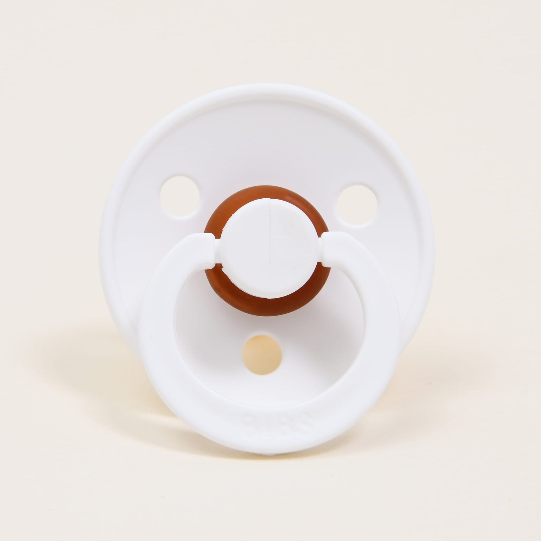A Bibs Pacifier from the White 2 Pack, crafted from natural rubber in a white and brown design with two circular holes in its base, is displayed against a simple beige background. Its classic appearance provides a comforting touch for little ones.