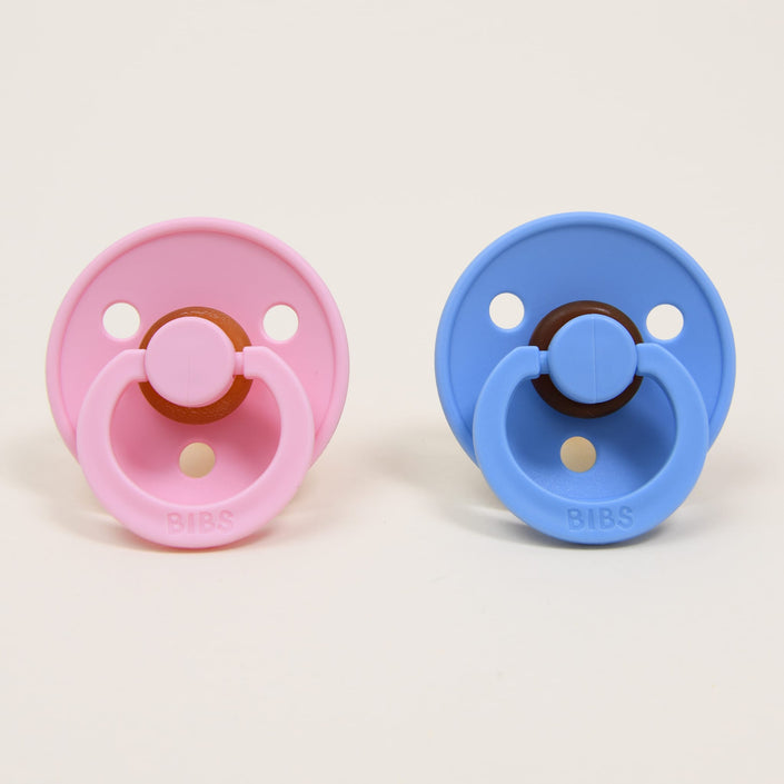 A pair of pacifiers from the Bibs Pacifier Set in Baby Pink and Sky Blue are positioned side by side against a simple white background. Made from natural rubber, each pacifier is designed with a circular shield adorned with "BIBS" text at the bottom, ideal for aiding infants in self-soothing. Crafted with attention to detail in Denmark.