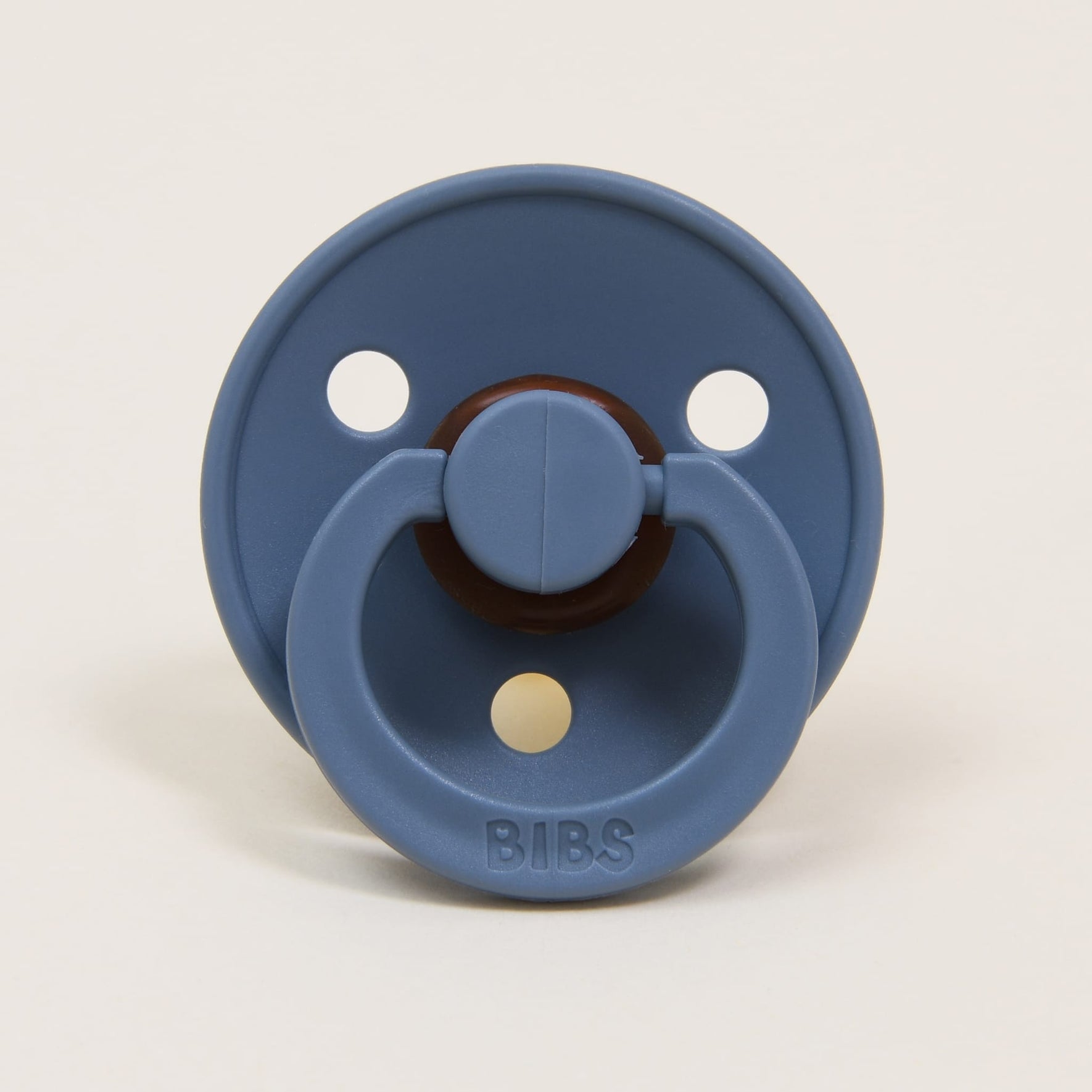 A petrol-colored natural rubber baby pacifier with a circular shield and three ventilation holes is pictured against a plain background. The brand name "BIBS," renowned in Denmark, is embossed on the handle, designed to help little ones self-soothe effectively.