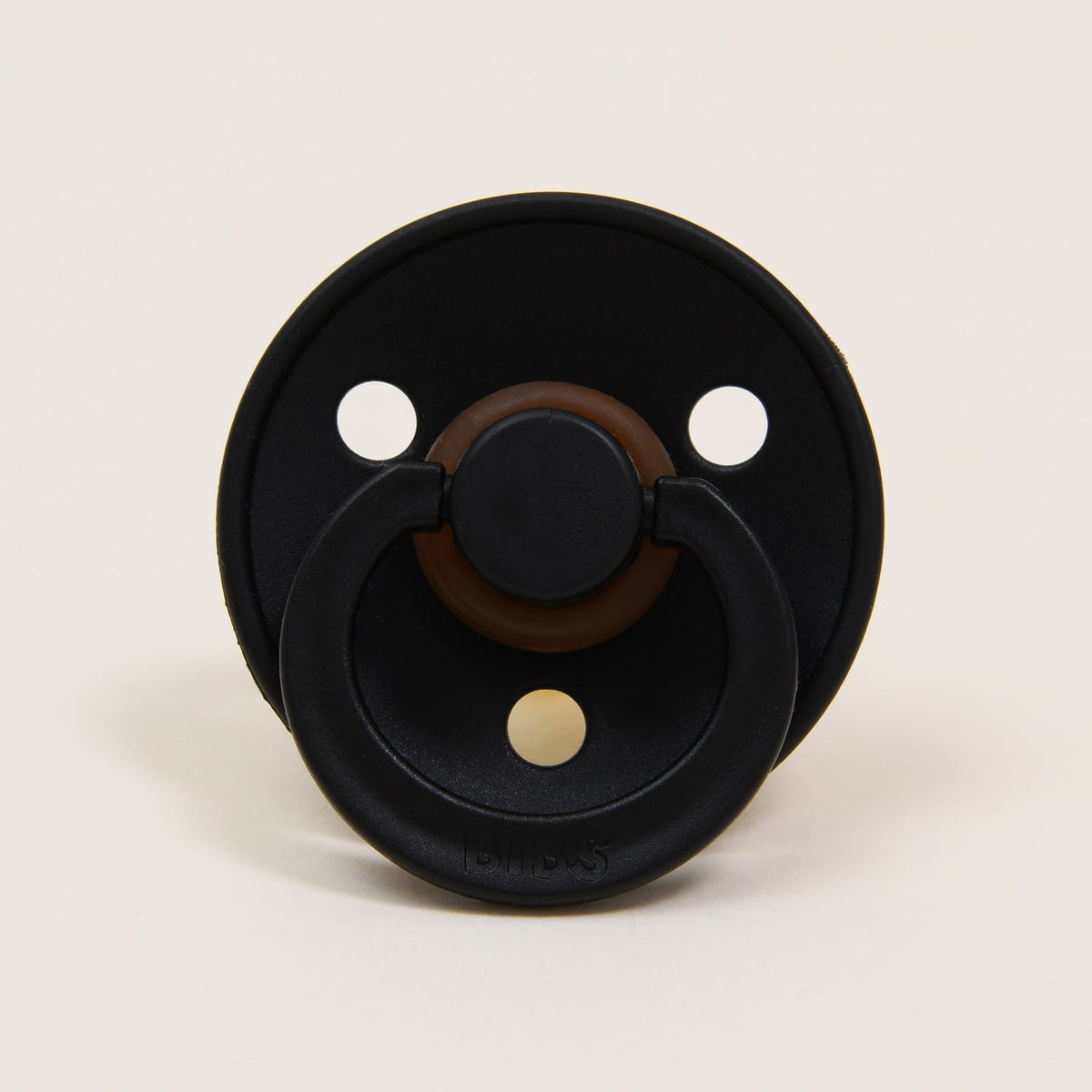 A Bibs Pacifier in black, with a round handle and circular shield, is positioned against a plain white background. Made in Denmark, this pacifier includes two small holes on either side of the handle, providing a self-soothing option for infants.