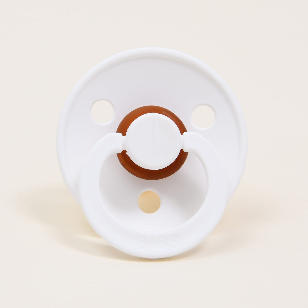 A Bibs Pacifier in white and ivory, crafted from natural rubber with a Danish-inspired round design featuring a brown center and two ventilation holes, rests on a plain white background—perfect for aiding your baby in self-soothing.