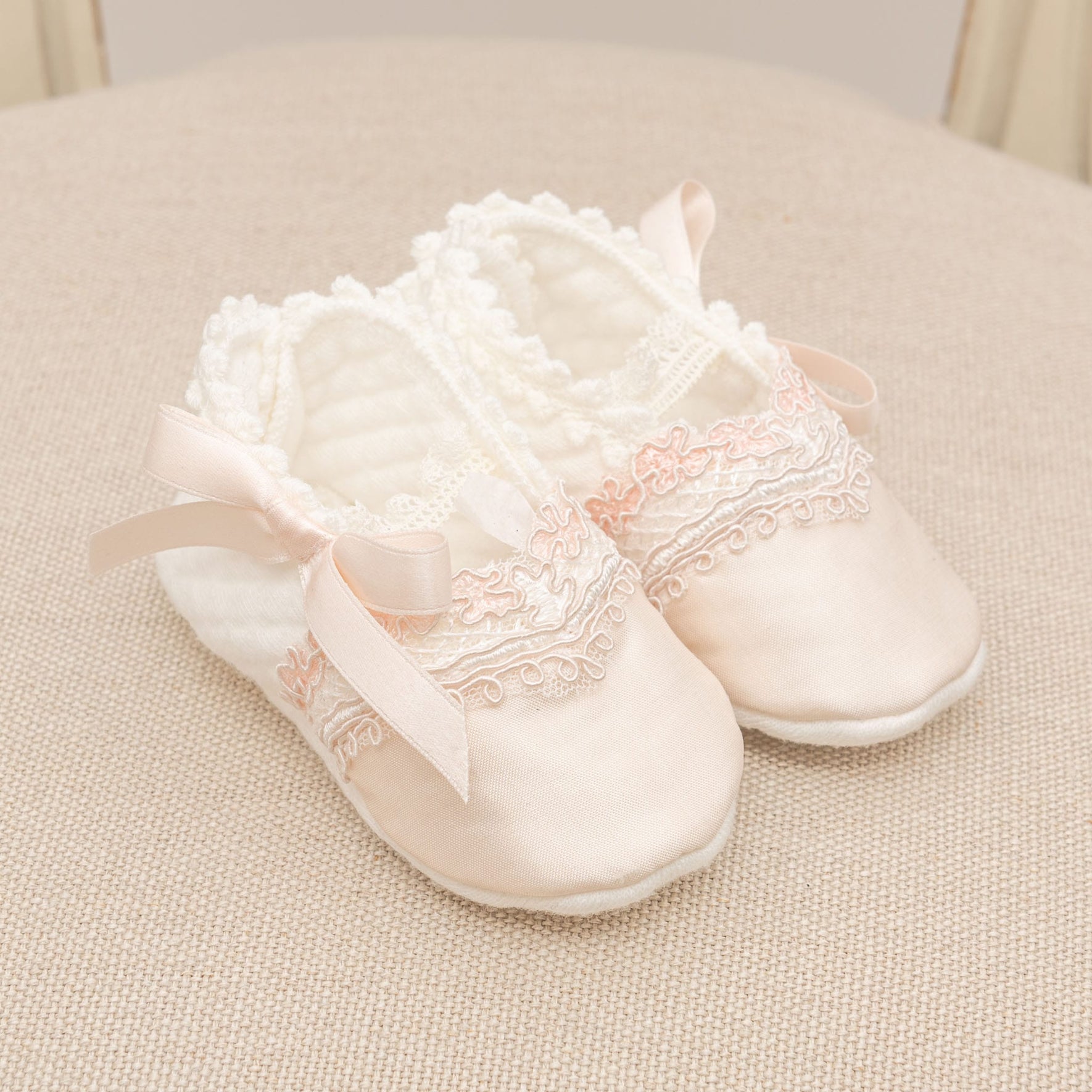 The Elizabeth Accessory Bundle - Save 15% features a pair of elegant pink baby shoes adorned with lace detailing and satin ribbons, ideal for enhancing a Christening outfit, displayed on a textured beige surface.