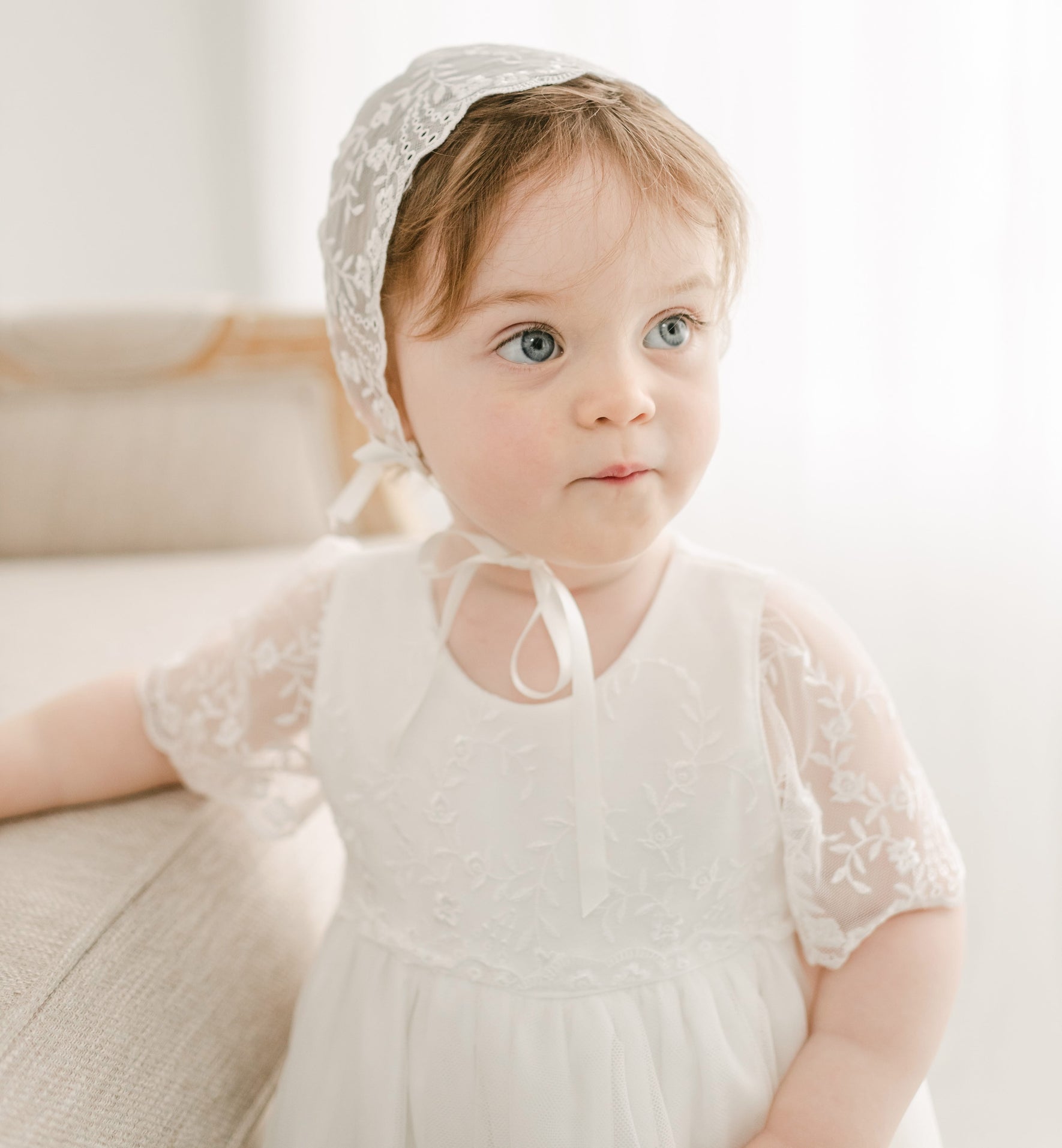 A baby girl wearing the Ella lace bonnet and full-length christening gown.