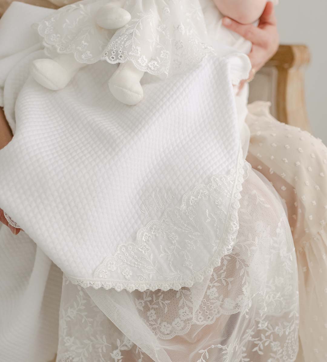 The Ella christening blanket draped over a mother and her baby daughter's lap.