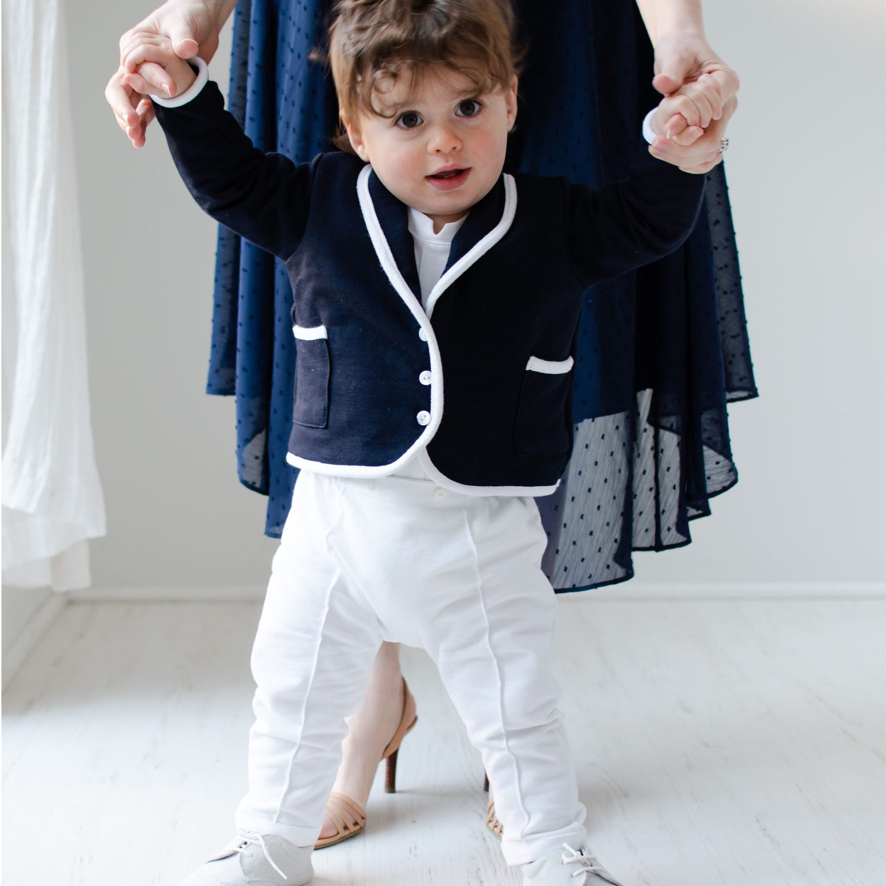 Baby boy holding on to his mother's hands. He is wearing the Elliott 3-Piece Suit, including the jacket, pants, and onesie.