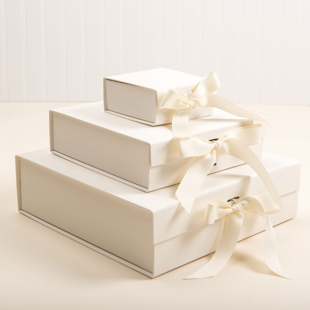 Three stacked ivory gift boxes of varying sizes, each adorned with a cream-colored ribbon bow. These elegant Gift Wrap | Ivory Gift Boxes are set against a neutral background, making them perfect for any special occasion.
