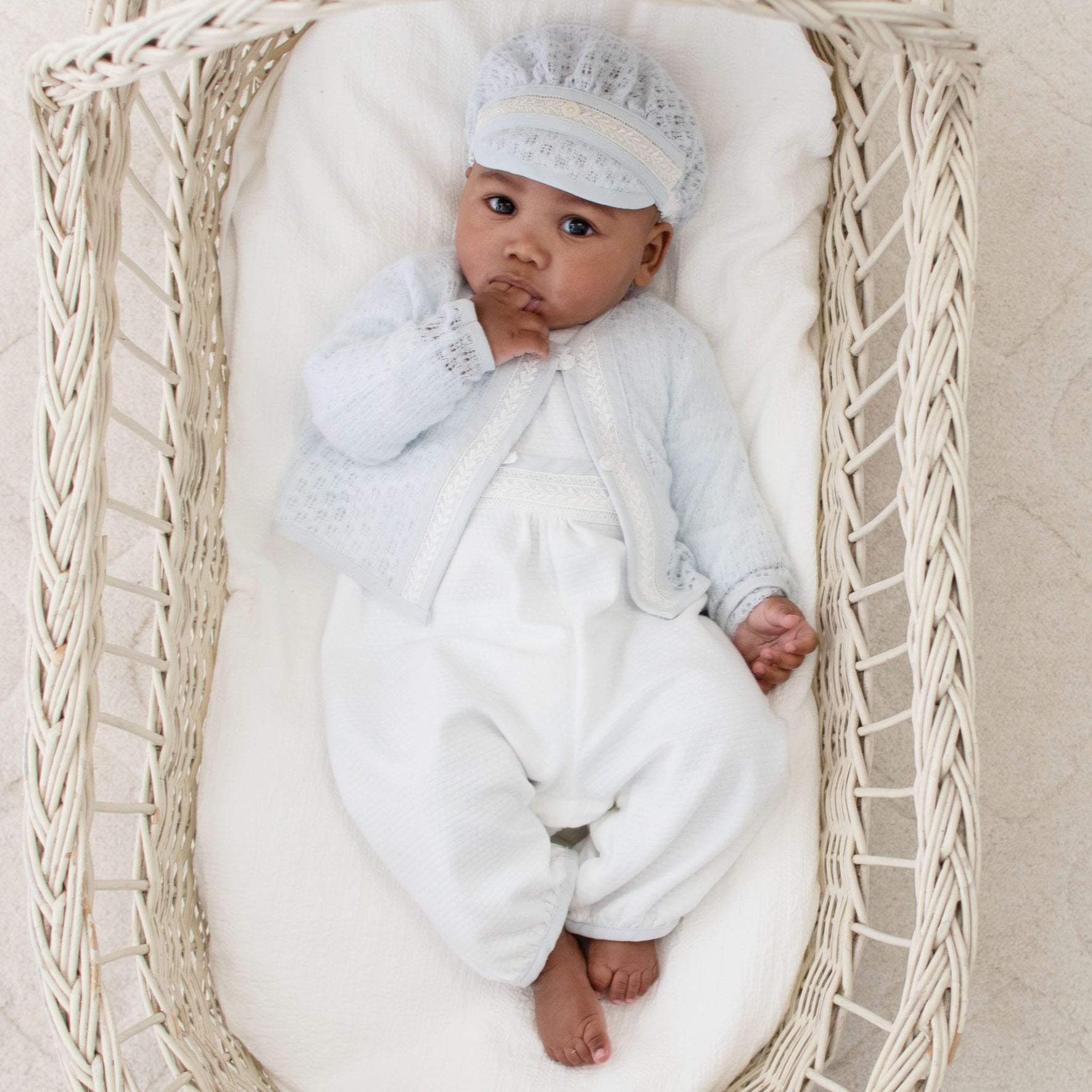 Infant dressed in the Harrison Long Sleeve Christening Romper with a coordinating lace sweater and cap for an intricate, refined appearance.