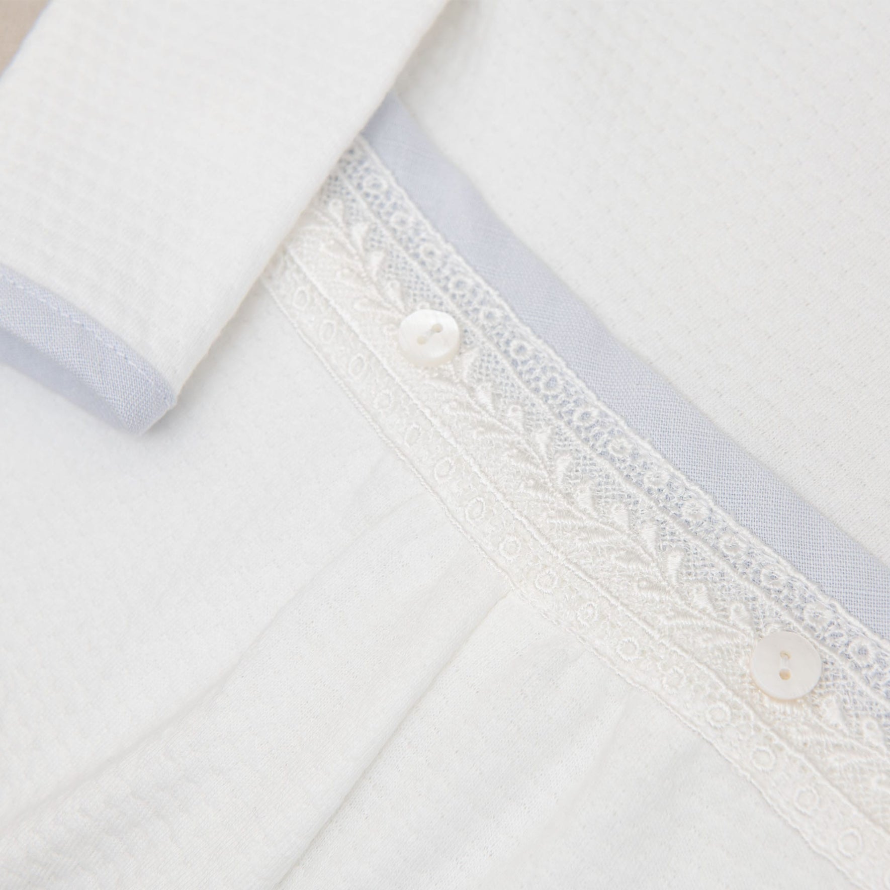 Detailed view of the Harrison Long Sleeve Christening Romper's waistband, featuring delicate lace accents and button details.
