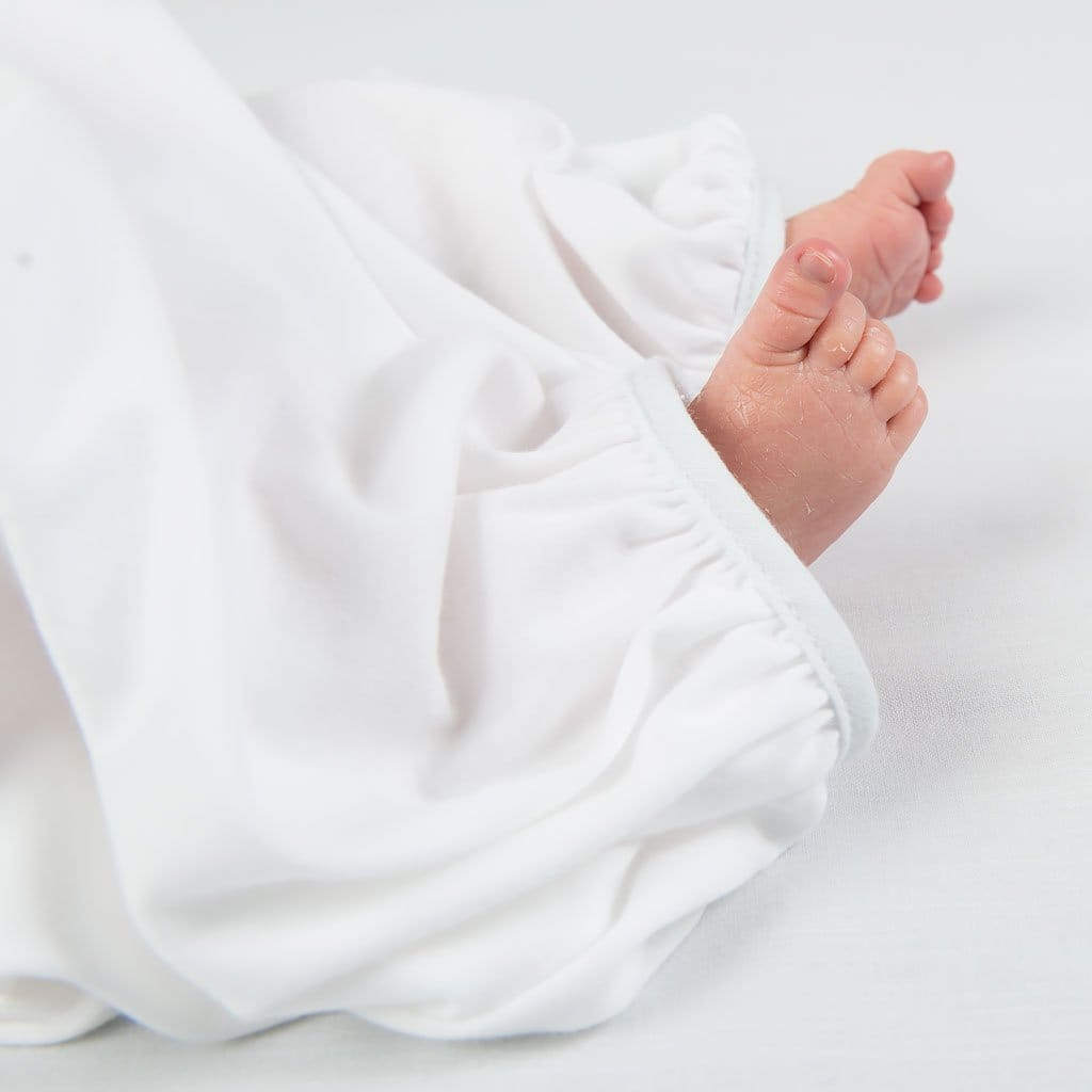 A tender close-up of baby feet resting against the soft hem of the Harrison Newborn Gown, showcasing its gentle fabric and tailored design.