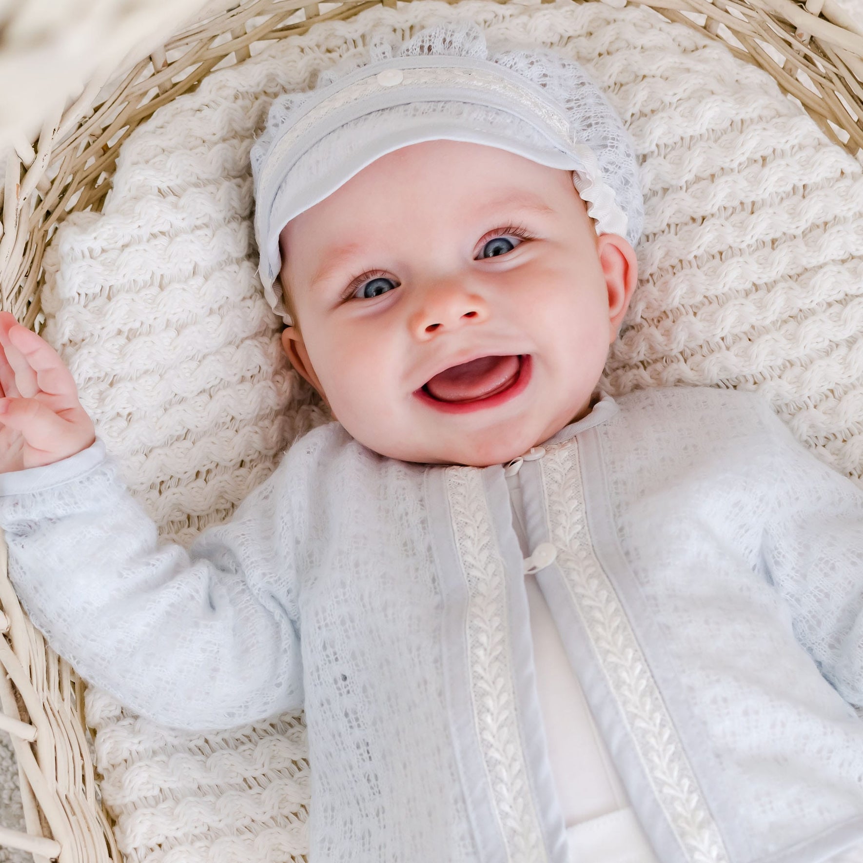 Baby lying in a wicker bassinet, smiling while dressed in the Harrison Sweater 3-Piece Pants Suit, highlighting the elegant lace-knit design.