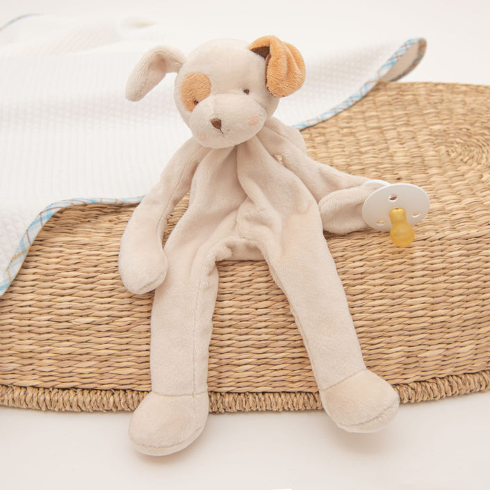 Presenting the Mason Puppy Buddy | Pacifier Holder, a plush toy resembling a beige dog with floppy ears made from soft velour. Ideal as a Christening gift, it sits on a woven mat next to a white blanket.