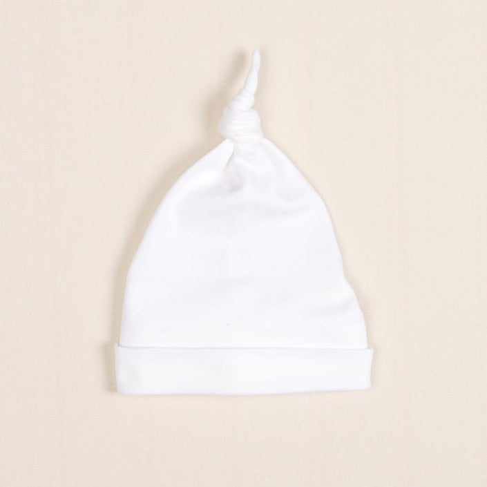 The Newborn Knotted Cap | Liam, a small white hat crafted from luxurious pima cotton, rests on a light beige background.
