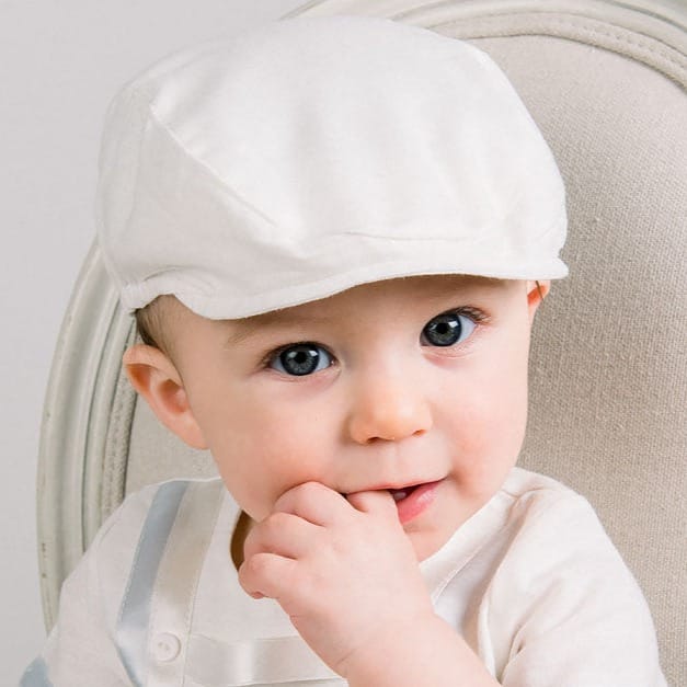 Baby boy wearing a Oliver Linen Newsboy Cap in white. It is made linen cotton blend and features a soft elastic band around the back.