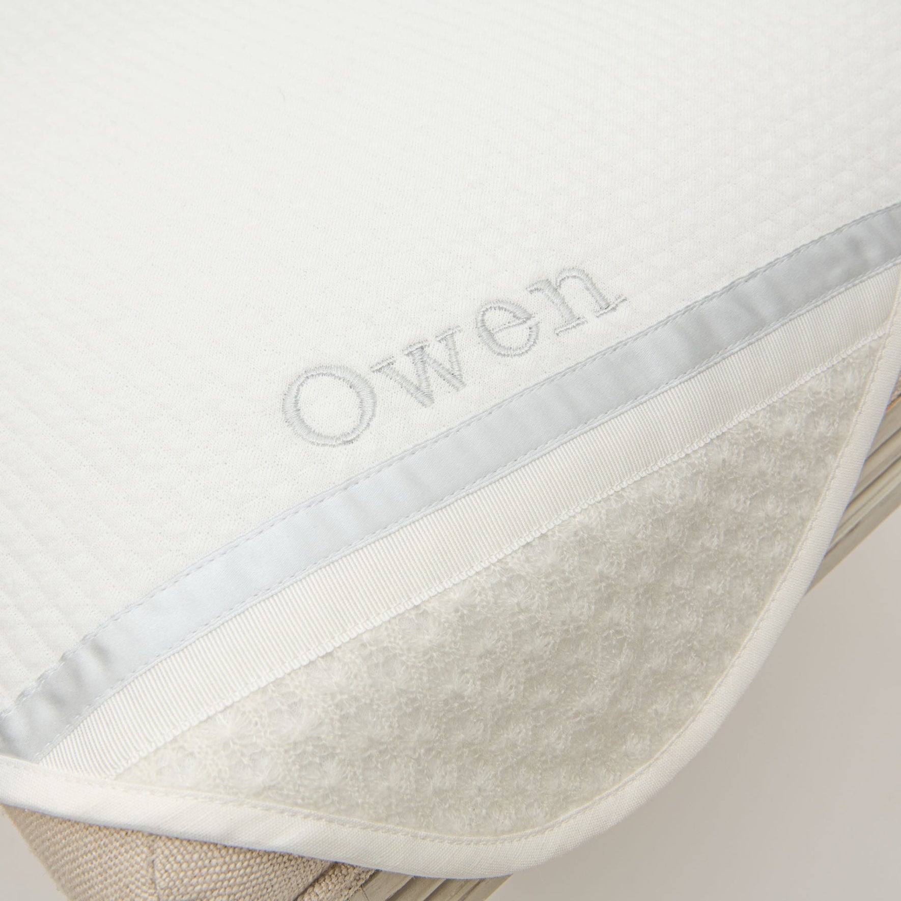 Closeup photo of the corner of the Owen Personalized Blanket. The corner features an ivory knit and the name "Owen" embroidered with light blue thread