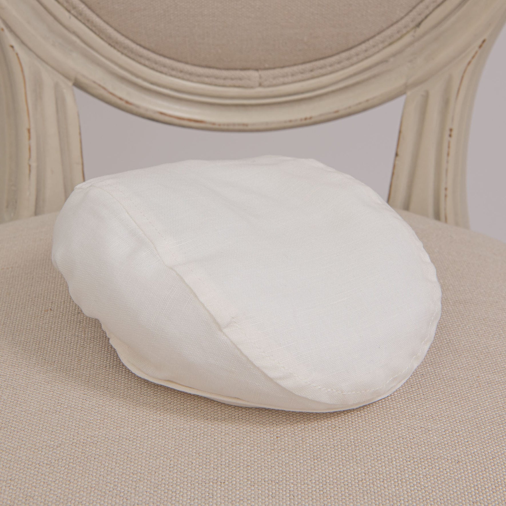 Flat lay photo of the Owen Linen Newsboy Cap on a chair. The hat is made from a Linen/cotton blend in light ivory