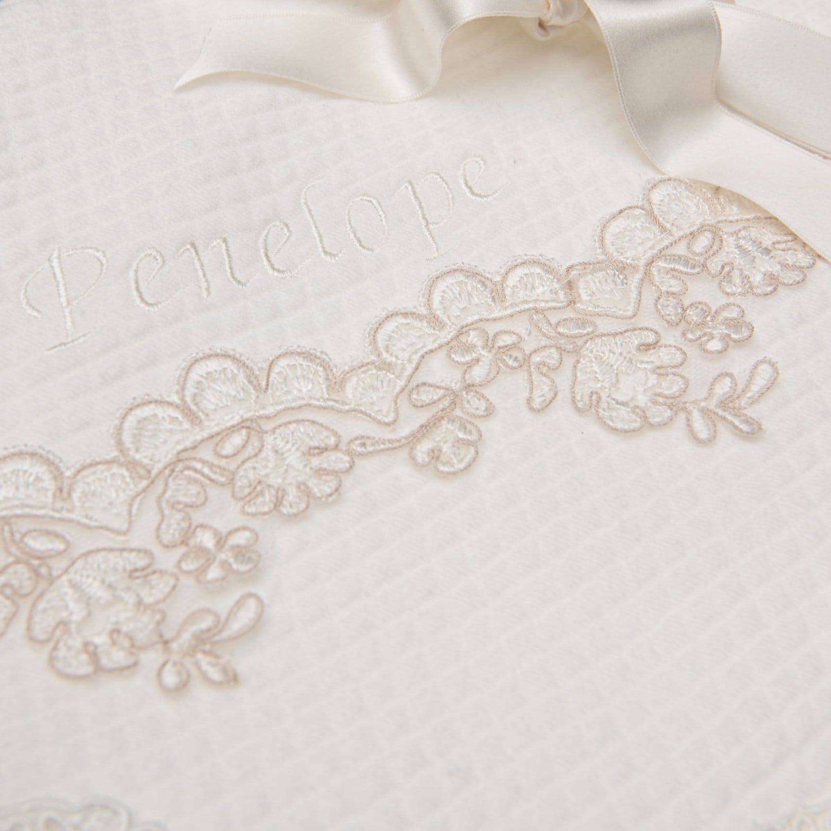 Baby girl baptism blanket wrapped neatly in a bow. The name Penelope is personalized on the corner of the blanket.