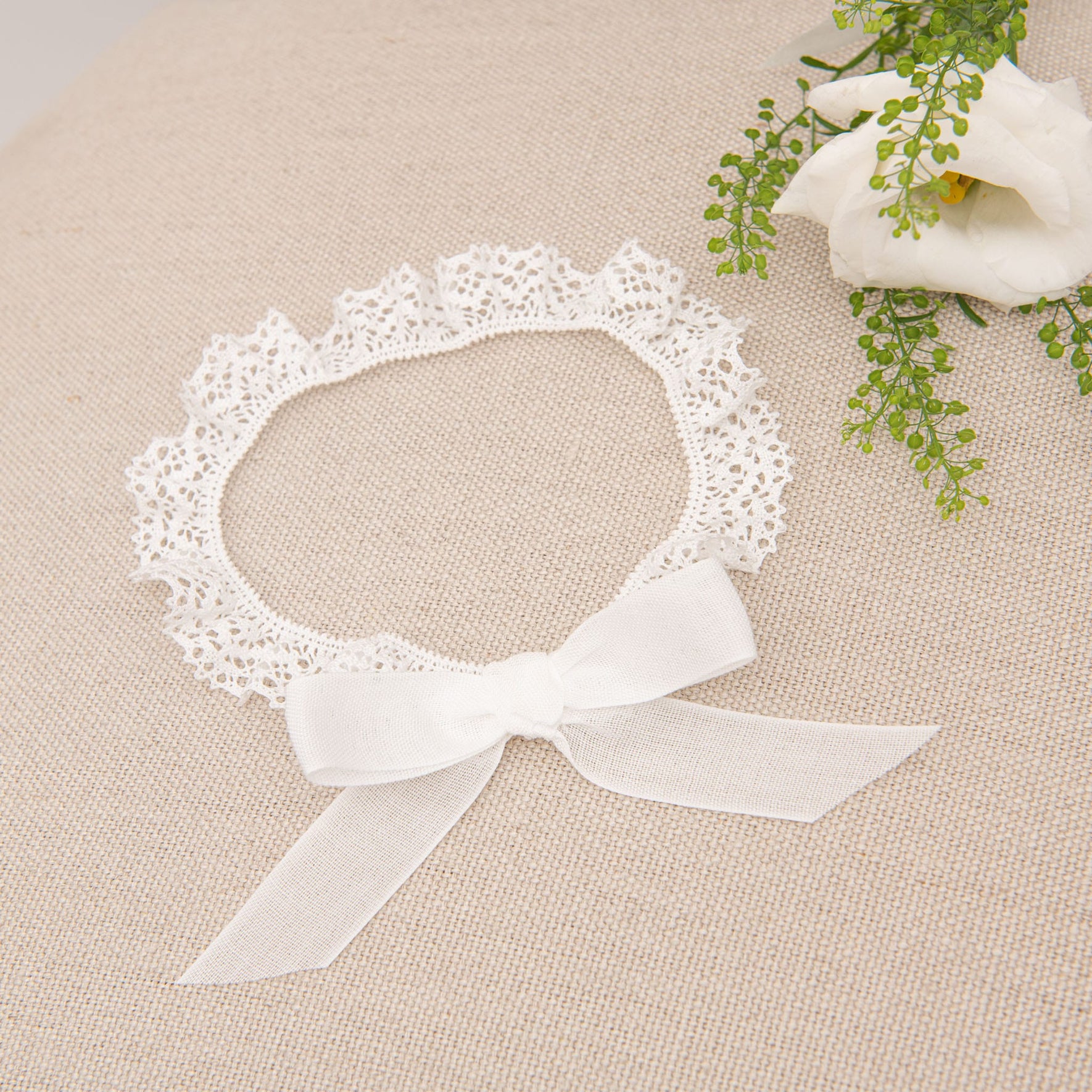 Detailed view of the Poppy Christening Headband, showcasing a white bow and lace accents, placed on a beige surface.