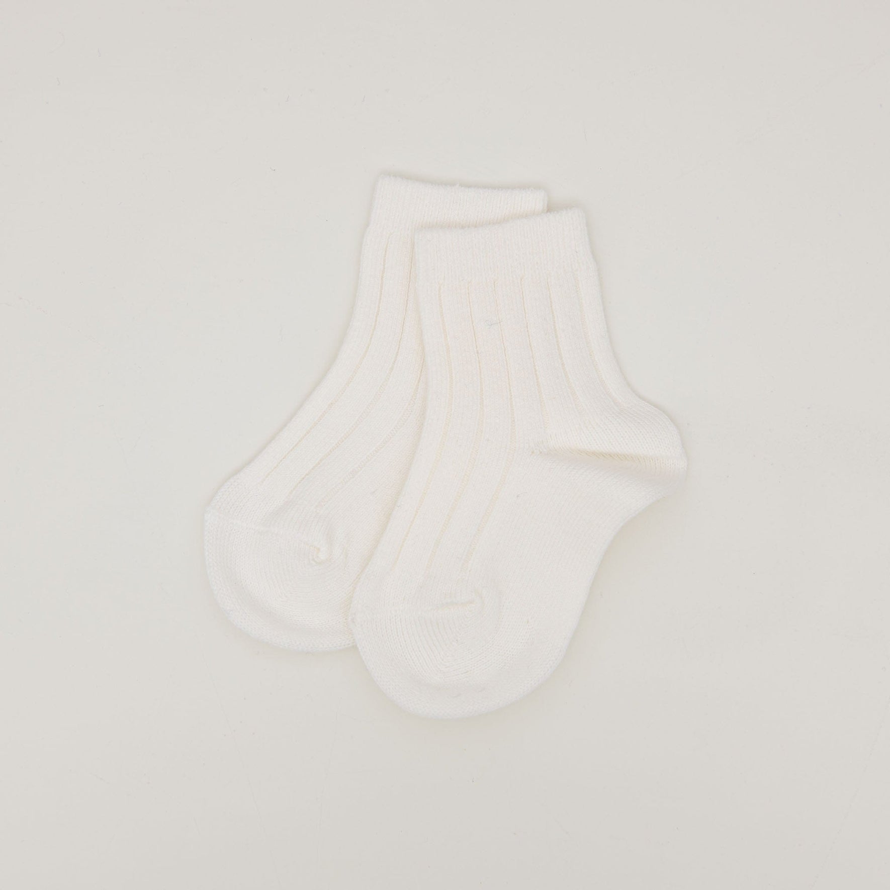 The Ribbed Socks, made from a soft cotton blend and featuring a minimalist ribbed pattern, are displayed flat on a simple, light-colored background with the heel and toe areas slightly visible.