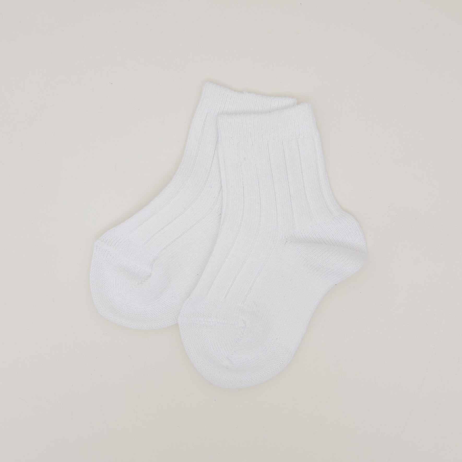 A pair of Ribbed Socks, crafted from a white cotton blend, rests on a simple light background. Featuring a ribbed pattern at the cuffs, these socks appear pristine and unworn, proudly made in Spain.