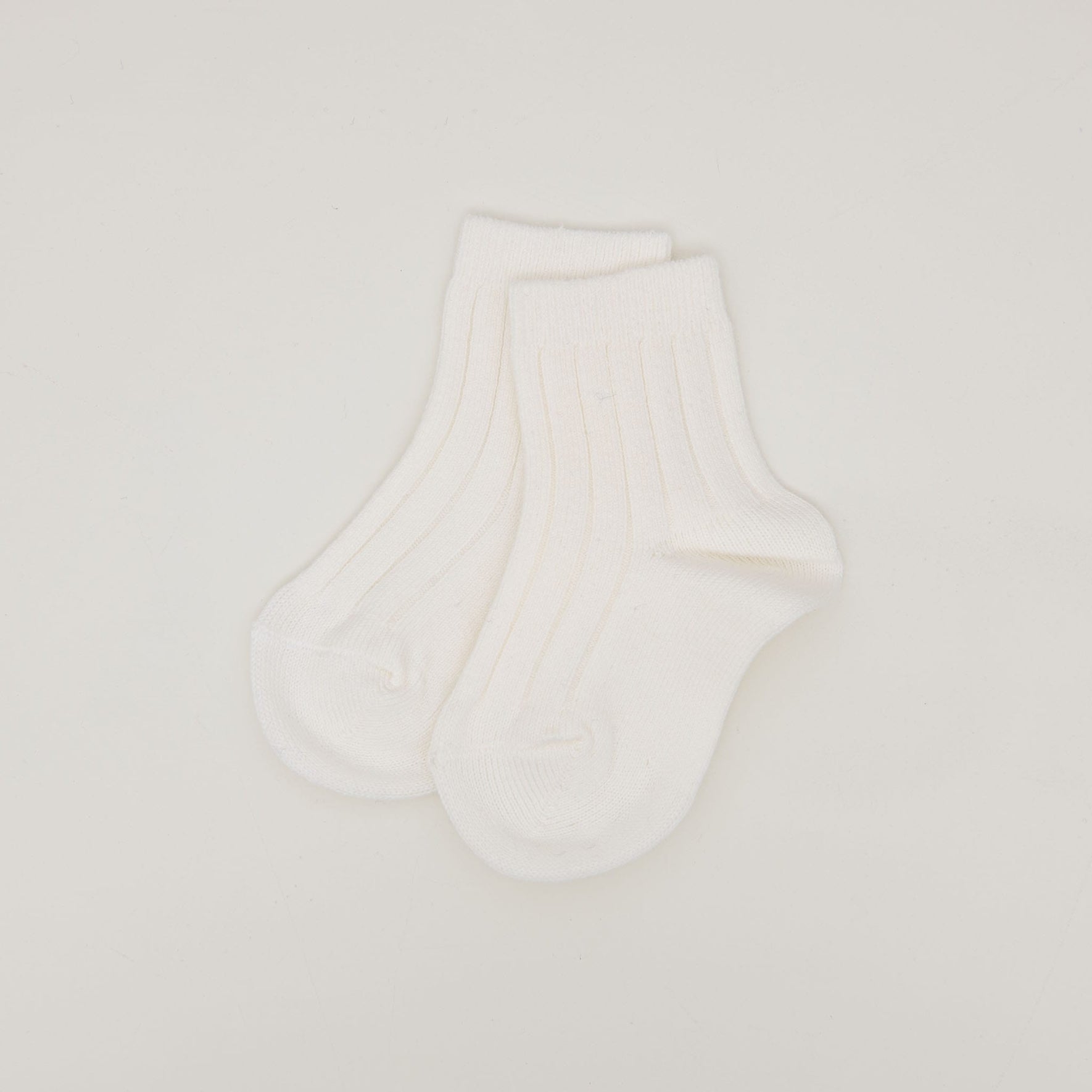 The Ribbed Socks, crafted with a cotton blend and featuring a white, ribbed pattern, are neatly positioned against a plain white backdrop. The ankle socks slightly overlap each other.