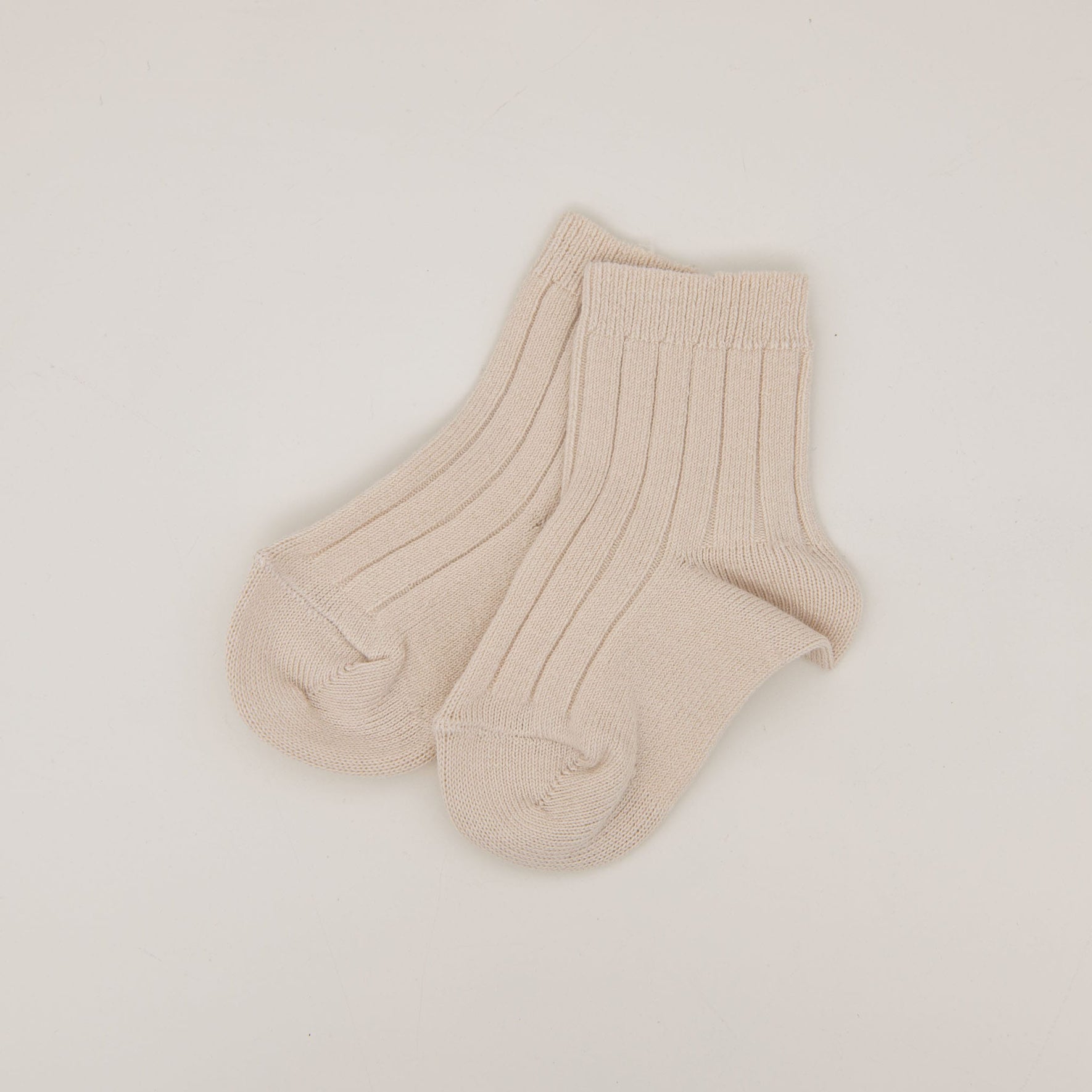 A pair of Ribbed Socks in a beige cotton blend is placed side by side on a plain white background, beautifully crafted and made in Spain.