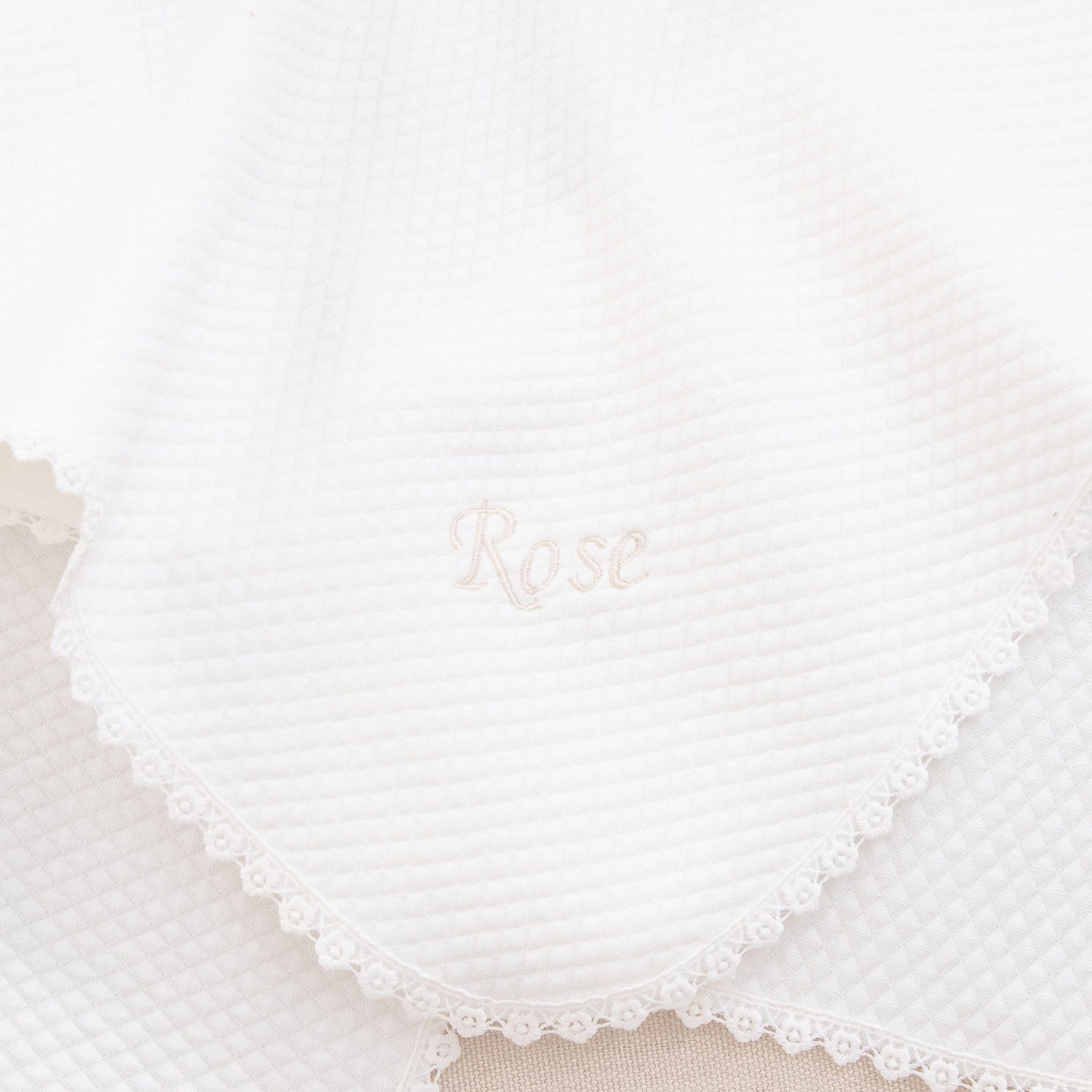A close-up of a white textured blanket featuring lace edging, ideal as part of the "Rose Accessory Bundle - Save 15%" baptism set. The name "Rose" is beautifully embroidered in the center.