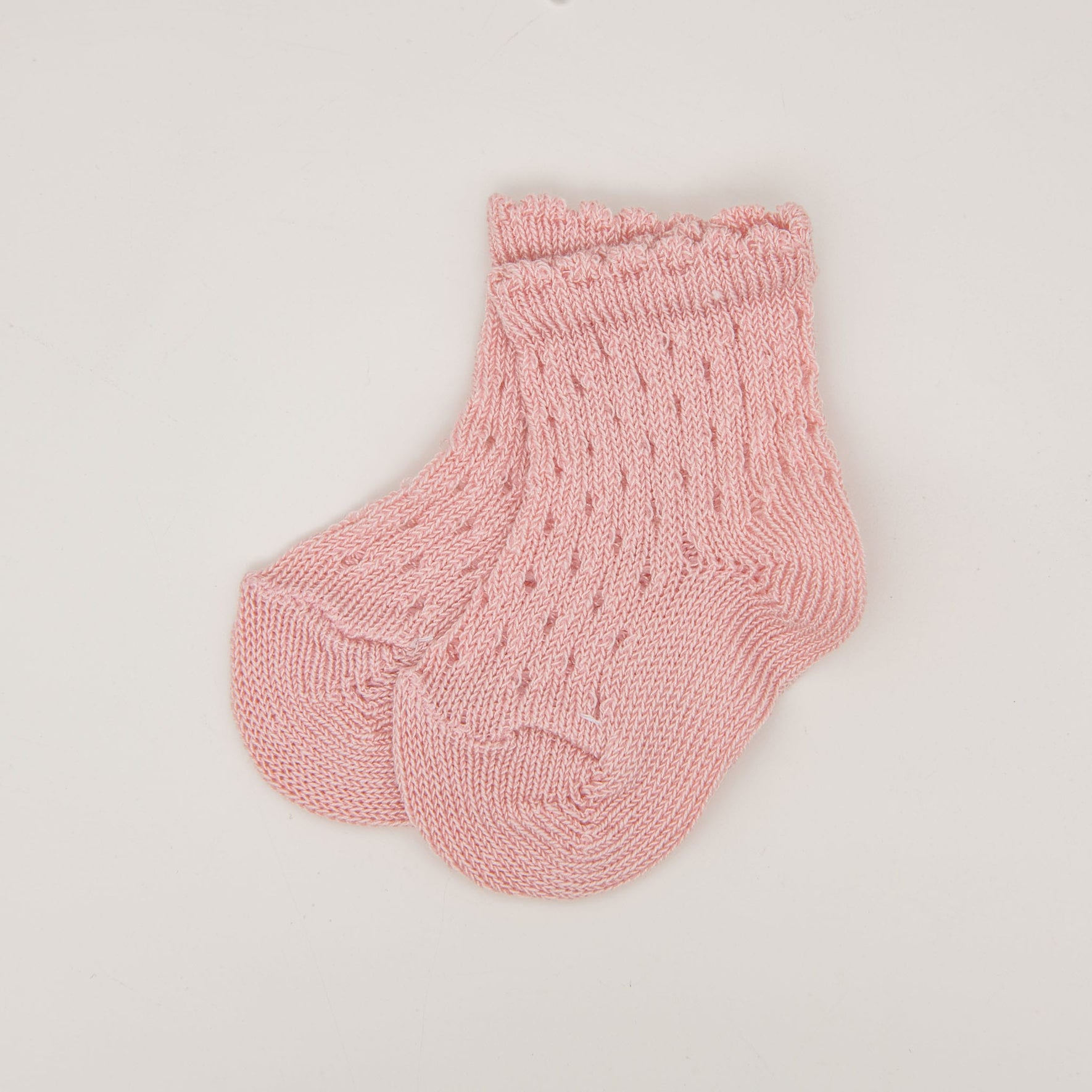 A pair of small Scallop Edge Crochet Socks in pink, made from 100% cotton with a textured pattern and delicate scalloped cuffs, neatly placed side by side on a plain white background.