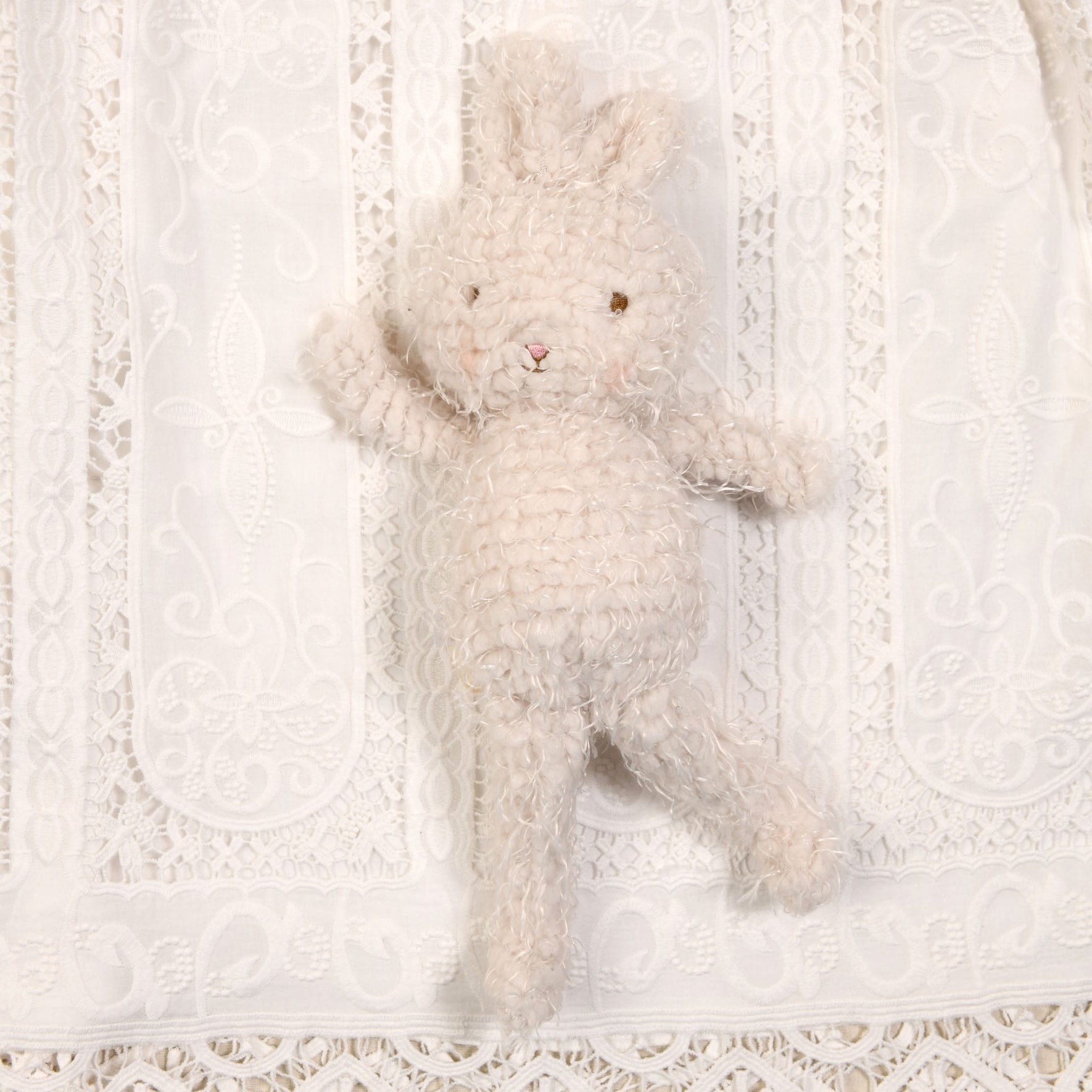 The Shaggy Bunny Friend, featuring pink cheeks and soft cream fur with a textured crochet design, is charmingly positioned against a white lace fabric background, making it an ideal baby shower gift.
