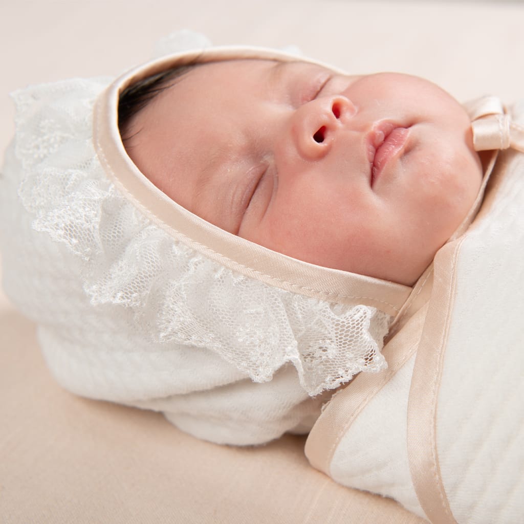 Close-up of a newborn baby peacefully sleeping while wearing the Tessa Quilted Christening Bonnet. The close-up view showcases the silk and lace detail edges on the bonnet.