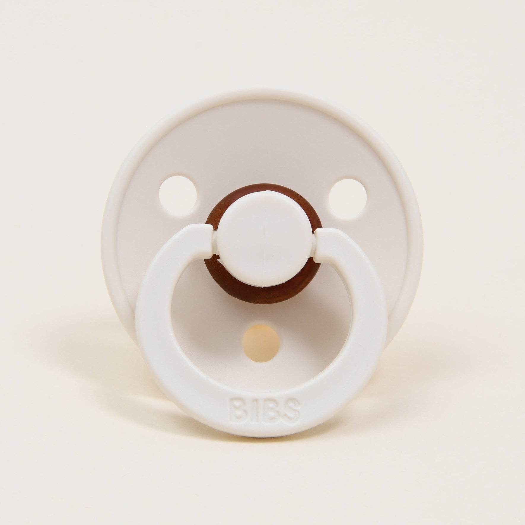 A pacifier from the Tessa Pacifier Set in an ivory color, made from natural rubber, features a circular shield with two holes and a handle. The brand name "BIBS" is embossed on the handle. Designed in Denmark, this pacifier is positioned against a plain, light background and is perfect for helping your baby self-soothe.