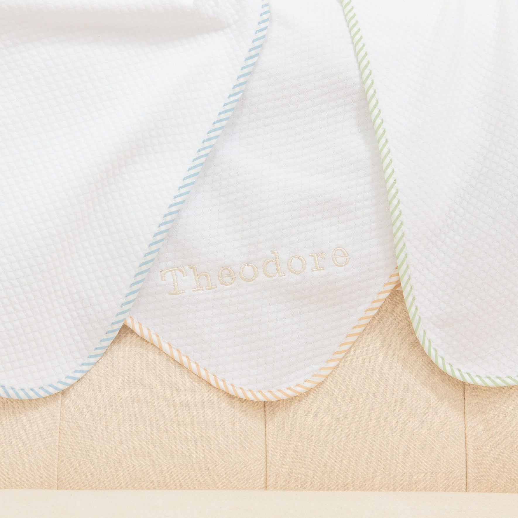 Detail of the corner of three Theodore Personalized Blankets in colors blue, green, and tan/white. Made from 100% textured cotton and featuring a ribbon corner and optional name embroidery.