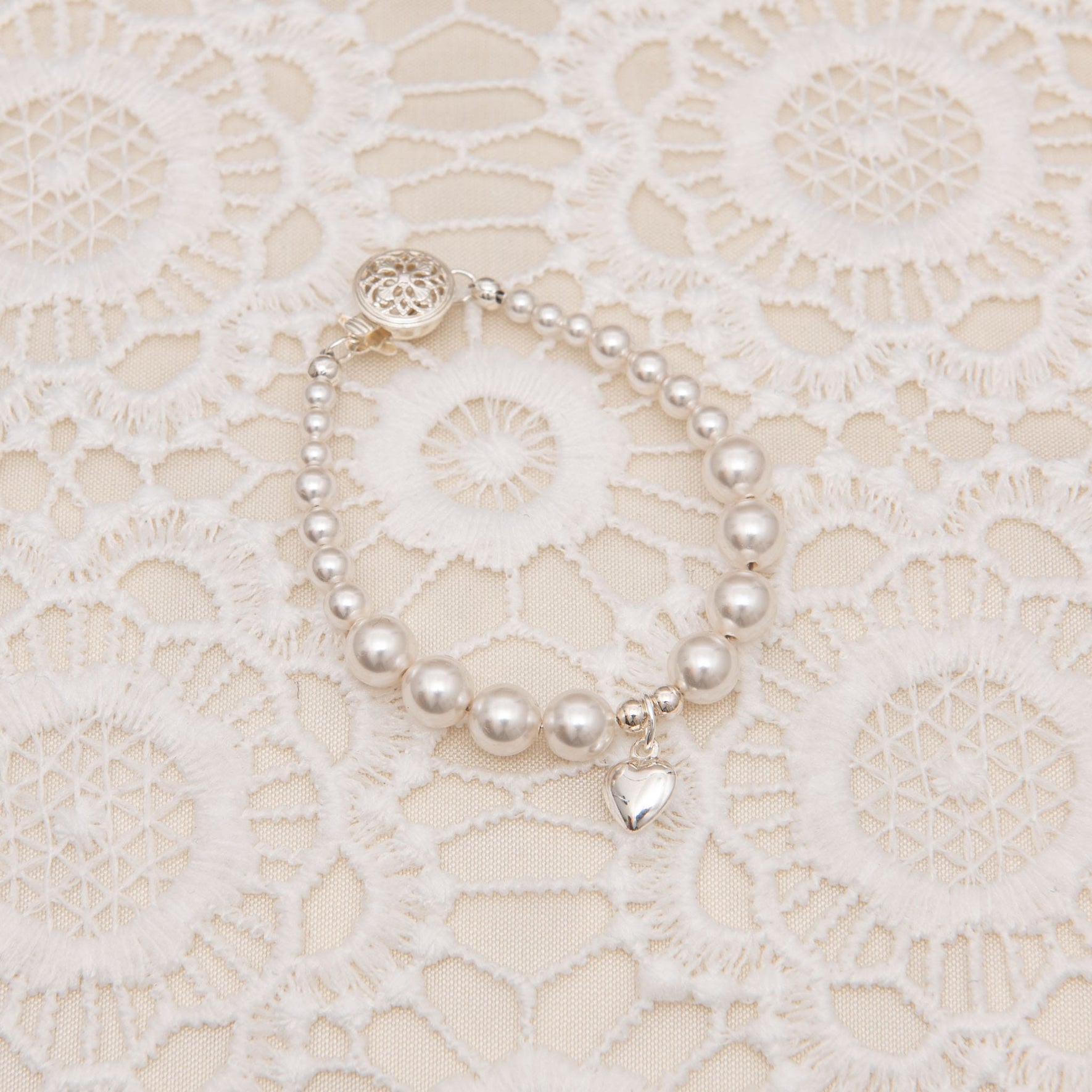 Close up of the White Luster Pearl Bracelet against a lace background. The bracelet features a silver heart charm, emphasizing its lustrous pearls and refined craftsmanship.
