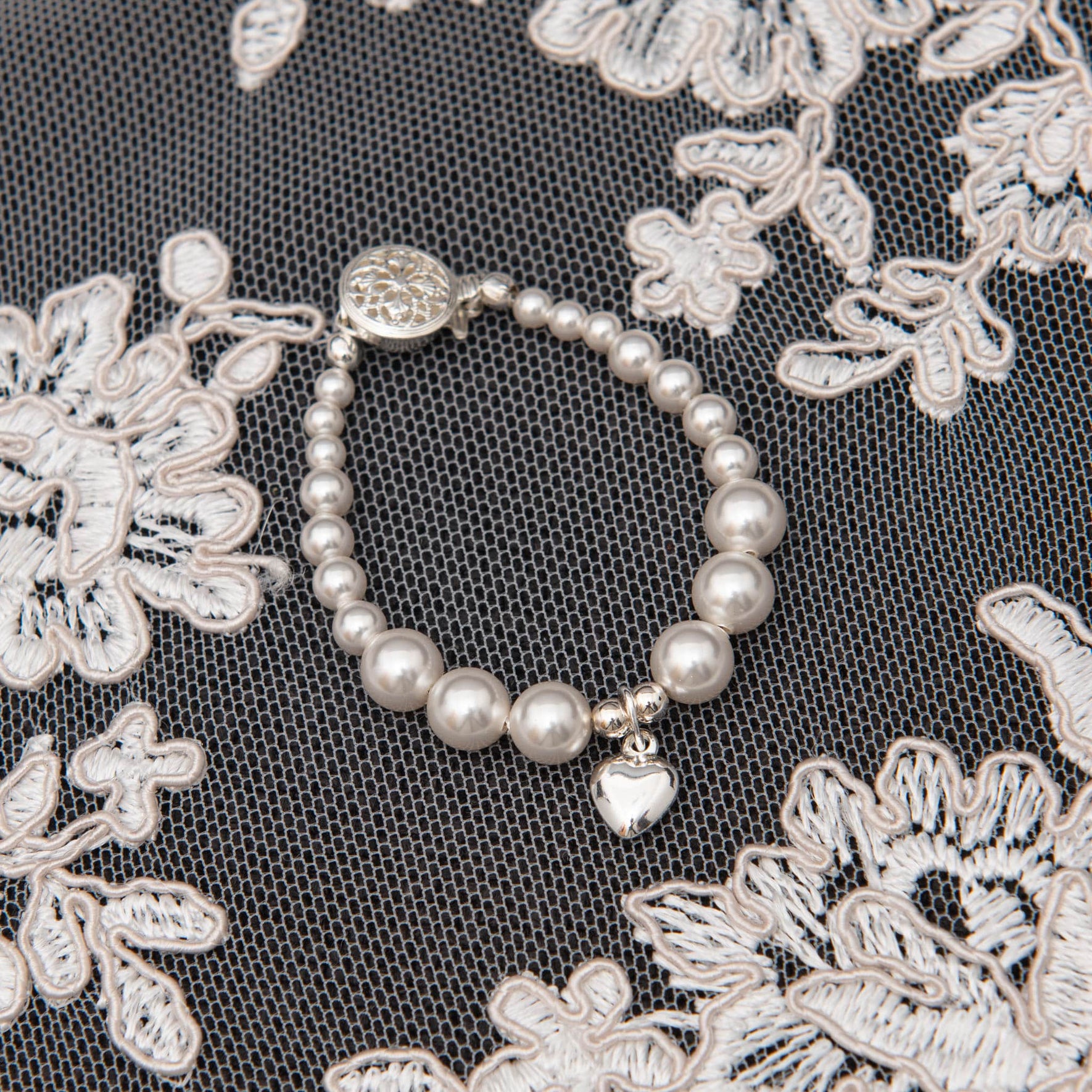 Flat lay photo of the white luster pearl heart bracelet with silver heart charm. 