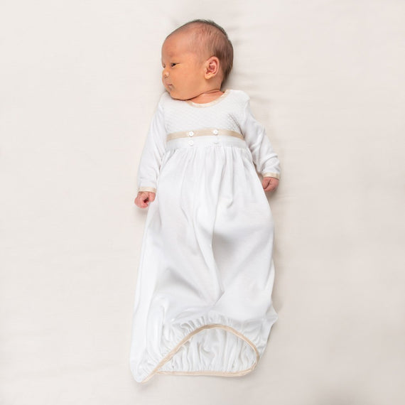Newborn baby boy wearing the Liam Cotton Newborn Gown crafted from soft white pima cotton, ivory quilted cotton bodice, and detailed with silk trim in a shade of champagne